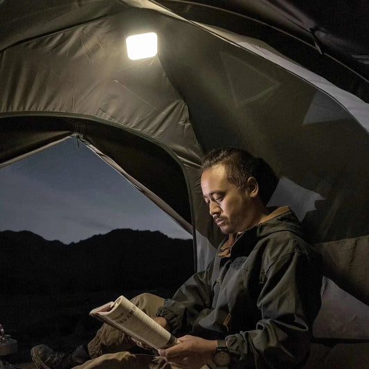 Versatile LED camping lantern illuminating a tent with a man reading, featuring adjustable brightness for outdoor adventures.