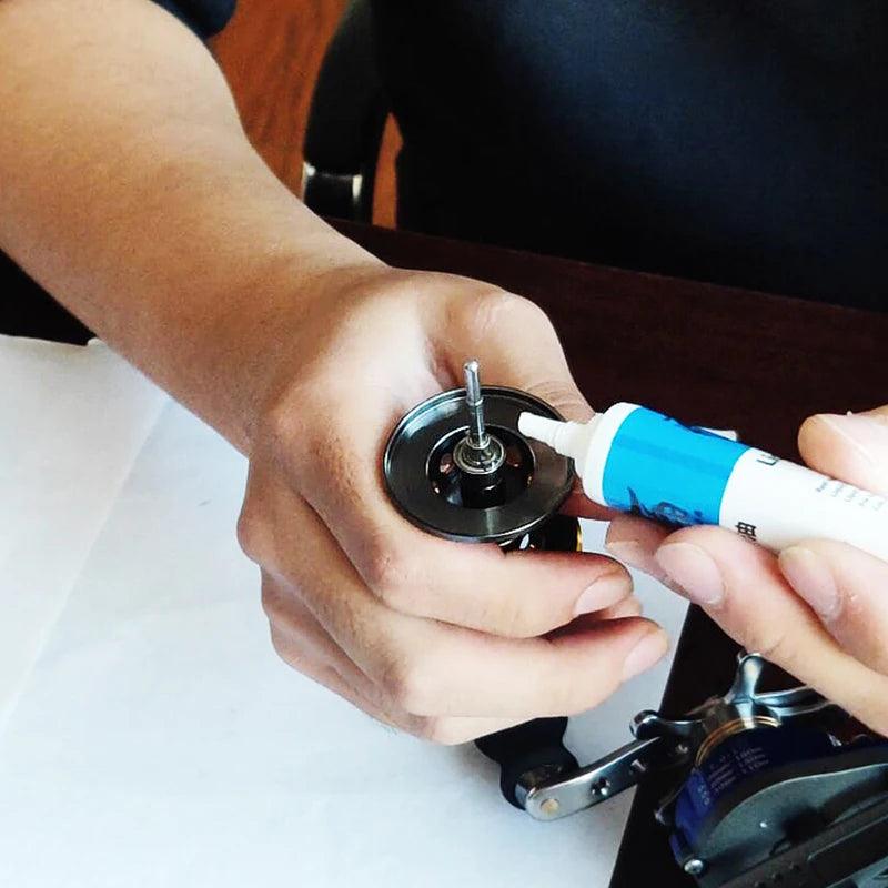 Person applying lubrication to a fishing reel with the Premium Reel Care Kit for smooth operation.